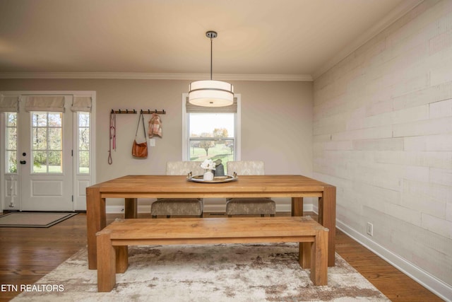 dining space featuring brick wall, ornamental molding, wood finished floors, and baseboards