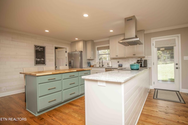 kitchen with stainless steel refrigerator with ice dispenser, light wood finished floors, wood counters, green cabinetry, and exhaust hood