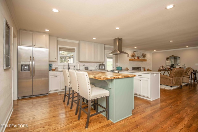 kitchen with island range hood, butcher block countertops, a kitchen island, open floor plan, and stainless steel fridge