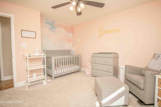 carpeted bedroom featuring a nursery area, ceiling fan, and baseboards