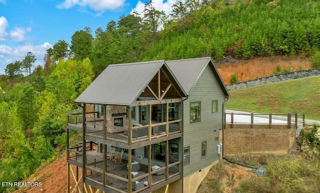 back of property with a forest view, metal roof, and a wooden deck