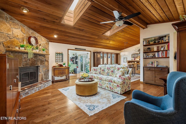 living room featuring vaulted ceiling with skylight, a stone fireplace, wood finished floors, wood ceiling, and a ceiling fan