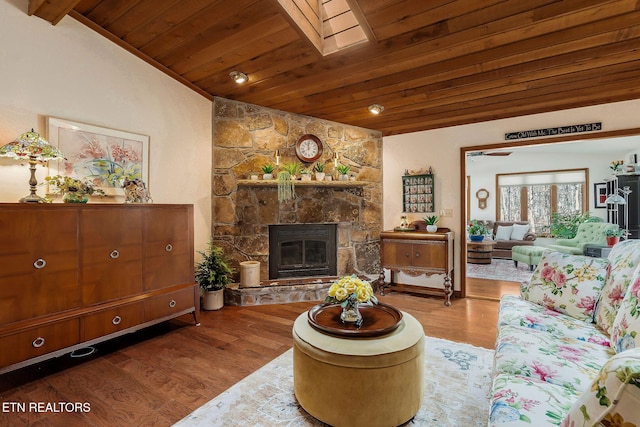 living area featuring wood ceiling, vaulted ceiling with skylight, wood finished floors, and a stone fireplace