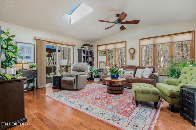 living room featuring light wood-type flooring, lofted ceiling with skylight, and ceiling fan