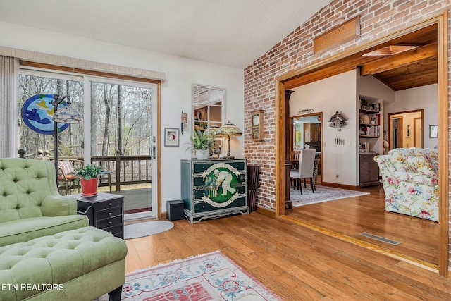 living area featuring wood-type flooring, visible vents, vaulted ceiling, and brick wall