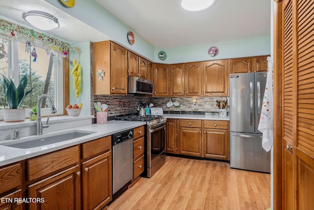 kitchen featuring brown cabinets, light wood finished floors, light countertops, appliances with stainless steel finishes, and a sink