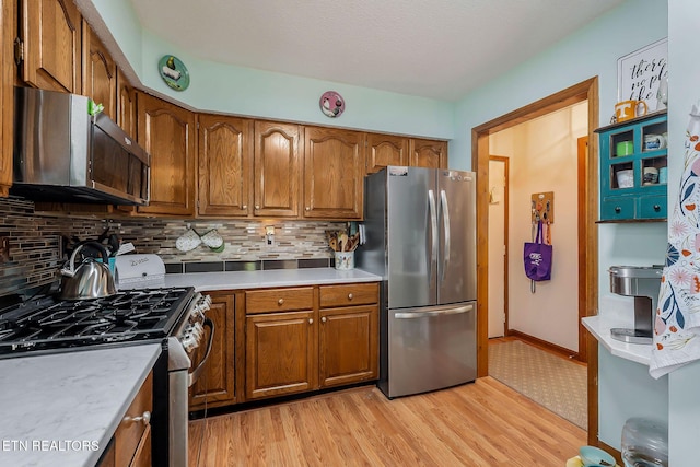 kitchen featuring light countertops, appliances with stainless steel finishes, brown cabinetry, and light wood-type flooring