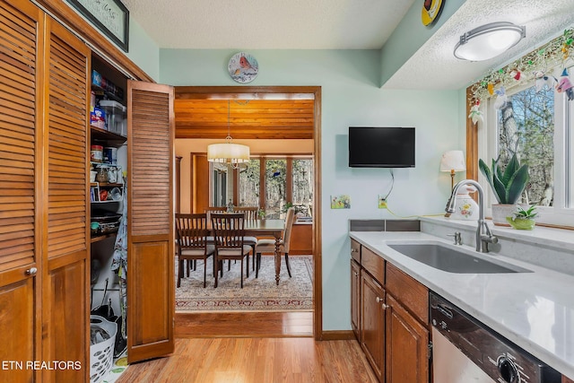 kitchen with a textured ceiling, dishwashing machine, a sink, and light wood-style flooring