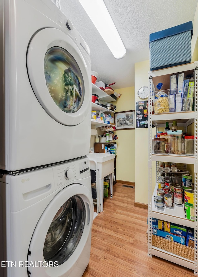 clothes washing area with a textured ceiling, baseboards, stacked washer / dryer, and wood finished floors