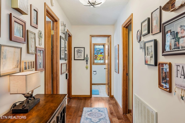 corridor featuring dark wood-style floors, visible vents, a textured ceiling, and baseboards