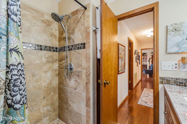 full bathroom featuring a tile shower, vanity, and wood finished floors