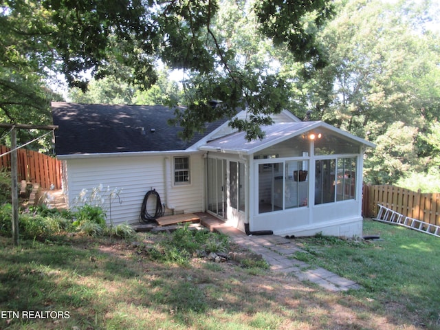 rear view of house with a sunroom, fence, and a lawn