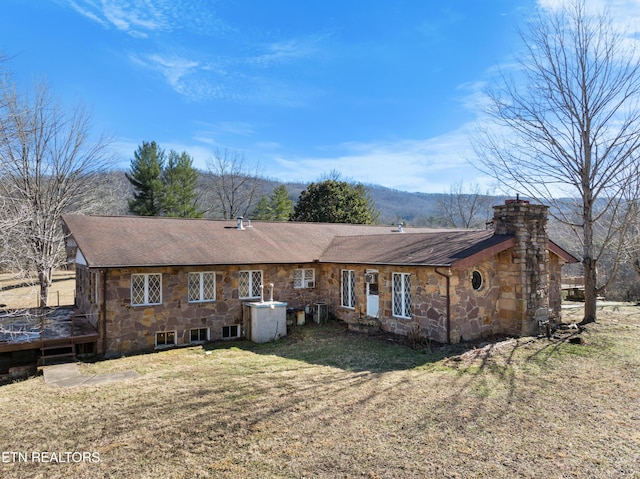 back of property featuring stone siding, a shingled roof, a chimney, and a yard