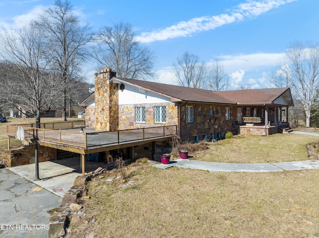 back of house with a chimney, a lawn, a deck, stone siding, and driveway