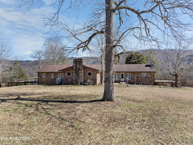 view of front of property featuring stone siding, a chimney, a mountain view, and a front yard