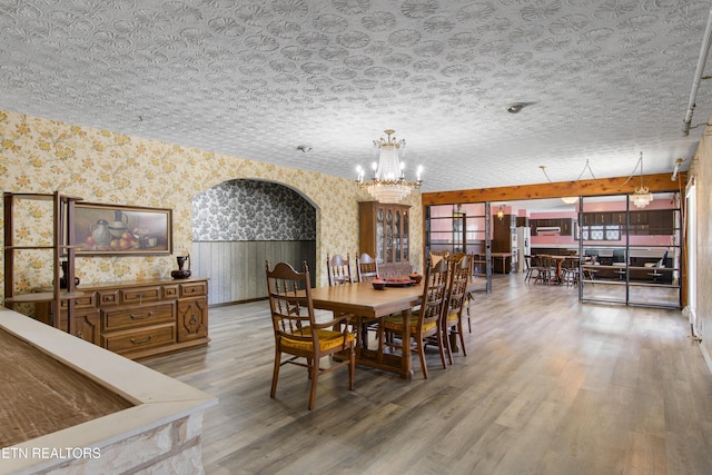 dining room featuring a chandelier, a textured ceiling, arched walkways, wood finished floors, and wallpapered walls