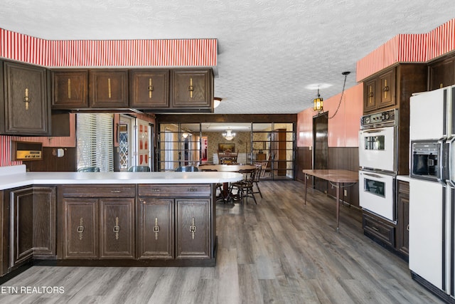 kitchen featuring a textured ceiling, a peninsula, white appliances, and wood finished floors