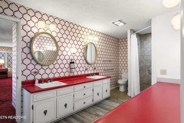 bathroom featuring double vanity, a sink, toilet, and wallpapered walls