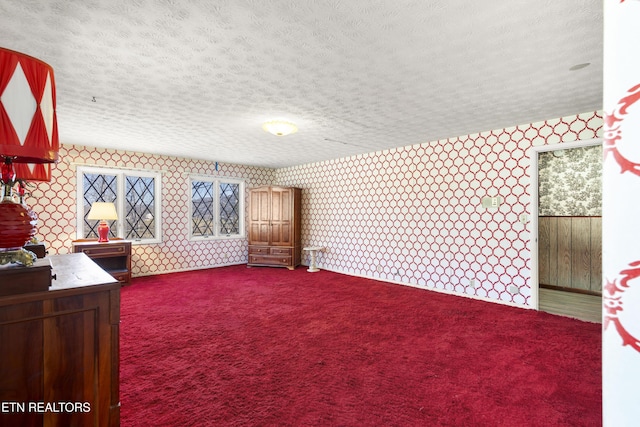 bedroom with a textured ceiling, dark colored carpet, and wallpapered walls