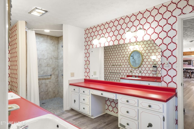 bathroom featuring tiled shower, wood finished floors, vanity, and wallpapered walls