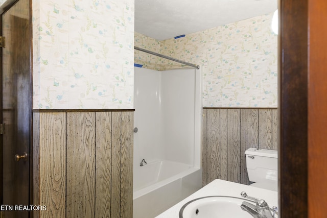 bathroom featuring wainscoting, a sink, shower / tub combination, and wallpapered walls