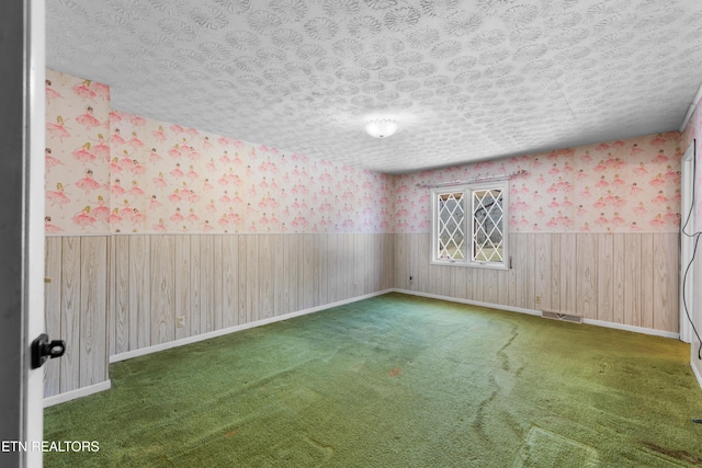 carpeted empty room with wallpapered walls, a textured ceiling, visible vents, and a wainscoted wall