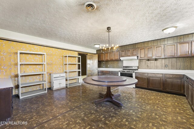 kitchen featuring wallpapered walls, visible vents, stainless steel gas range, a textured ceiling, and under cabinet range hood