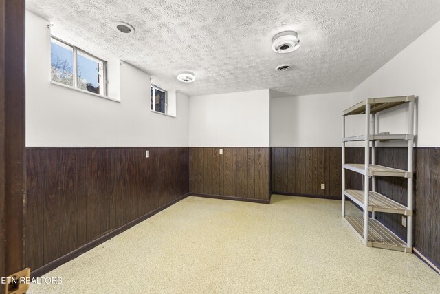 basement with a textured ceiling, wood walls, and wainscoting