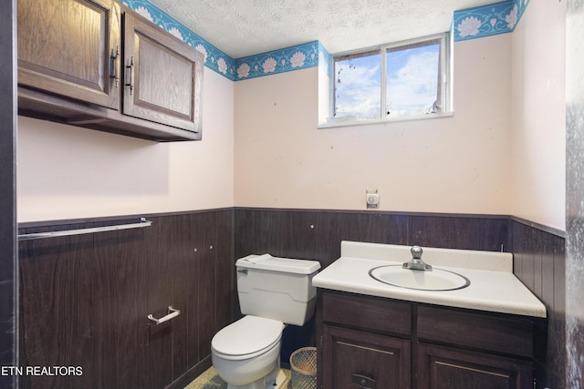 bathroom featuring wainscoting, a textured ceiling, toilet, and vanity