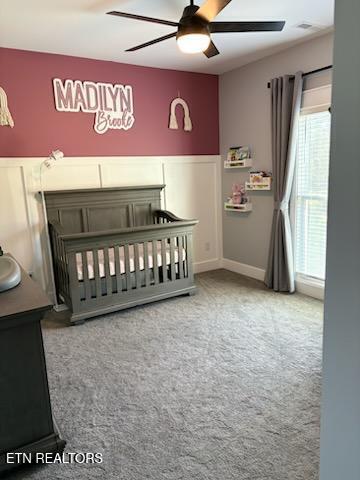 carpeted bedroom featuring a crib and ceiling fan