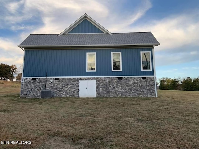 view of side of home featuring a shingled roof, stone siding, and a yard