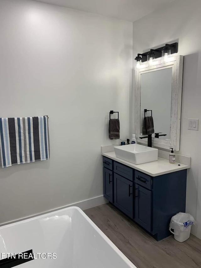 bathroom with a freestanding tub, baseboards, wood finished floors, and vanity