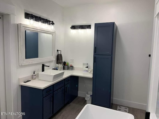 bathroom with a freestanding tub, baseboards, wood finished floors, and vanity