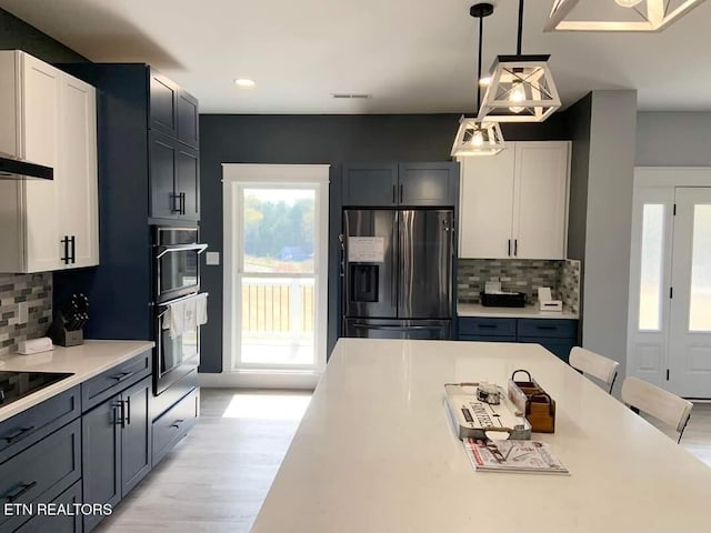 kitchen with double wall oven, light countertops, light wood-type flooring, stainless steel fridge with ice dispenser, and decorative light fixtures