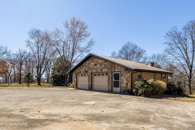 view of side of home with driveway, a garage, stone siding, a chimney, and brick siding