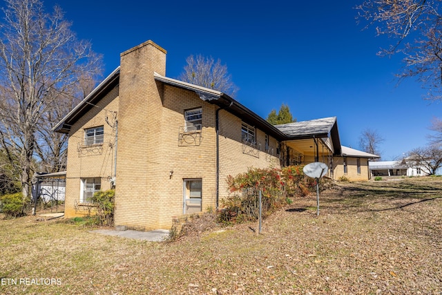 view of side of home featuring brick siding, a lawn, and a chimney