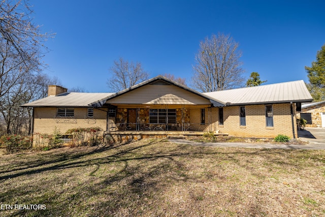 ranch-style home featuring a porch, brick siding, a chimney, and a front lawn