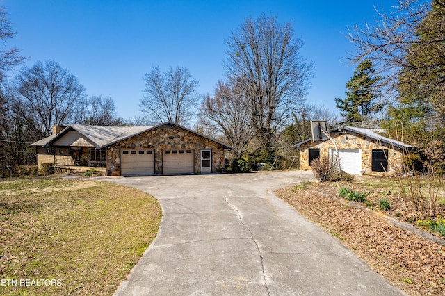 view of property exterior with a yard, a chimney, an attached garage, stone siding, and driveway