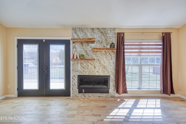 unfurnished living room with french doors, a fireplace, baseboards, and wood finished floors