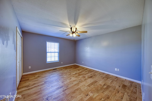 spare room with ceiling fan, light wood-style flooring, baseboards, and a textured ceiling