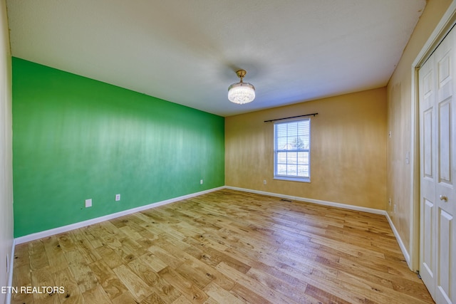 empty room featuring a notable chandelier, baseboards, and wood finished floors