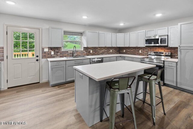 kitchen with appliances with stainless steel finishes, a sink, light wood-style flooring, and a kitchen bar