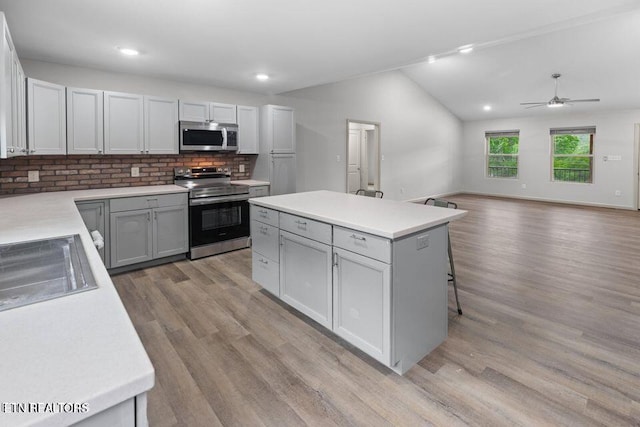 kitchen featuring a center island, light wood finished floors, lofted ceiling, light countertops, and appliances with stainless steel finishes