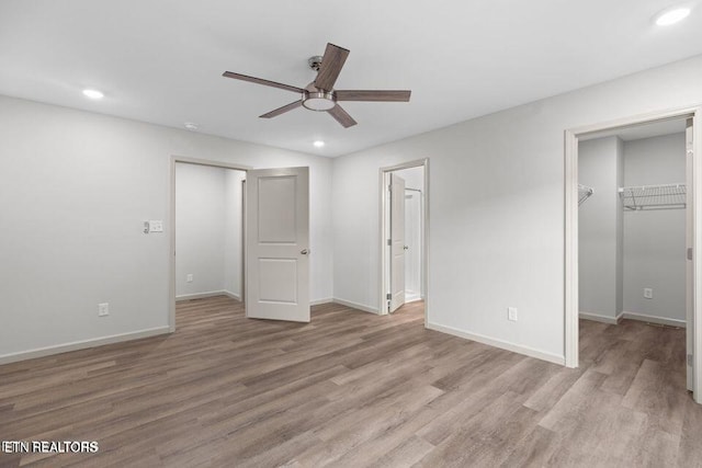 unfurnished bedroom with a spacious closet, baseboards, wood finished floors, and recessed lighting