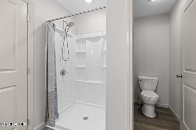 bathroom featuring wood finished floors, a shower stall, toilet, and baseboards