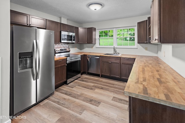 kitchen with stainless steel appliances, light wood-style flooring, a sink, dark brown cabinets, and butcher block countertops