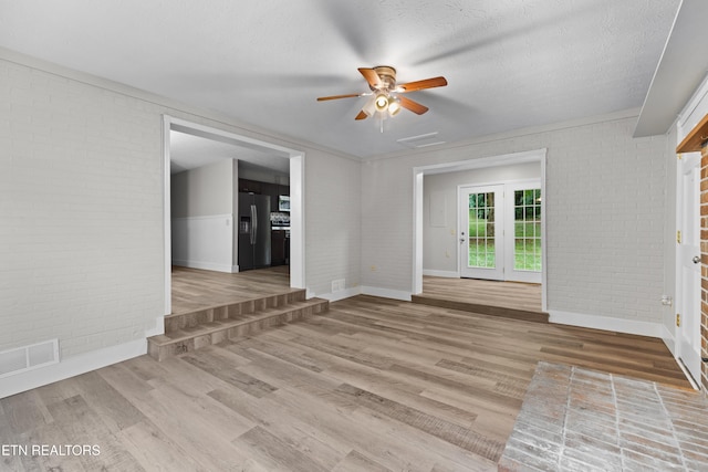 unfurnished living room with visible vents, a textured ceiling, brick wall, and wood finished floors