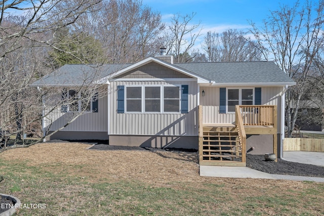 view of front facade with a shingled roof, stairs, board and batten siding, a chimney, and a front yard