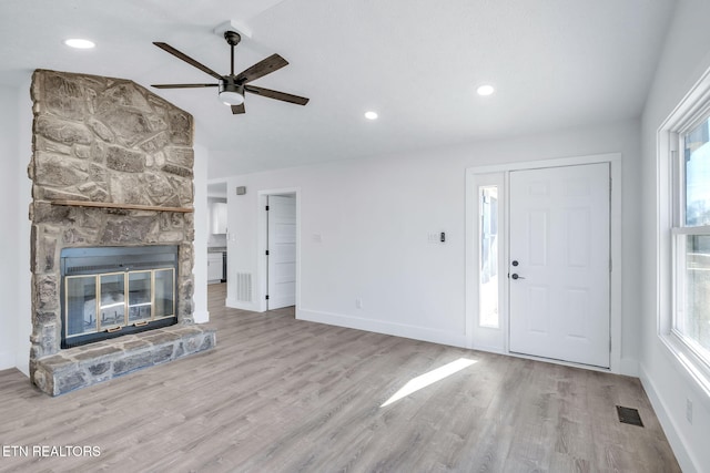 unfurnished living room featuring a healthy amount of sunlight, visible vents, wood finished floors, and a stone fireplace