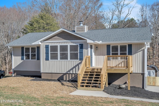 rear view of house featuring a wooden deck, roof with shingles, and a chimney